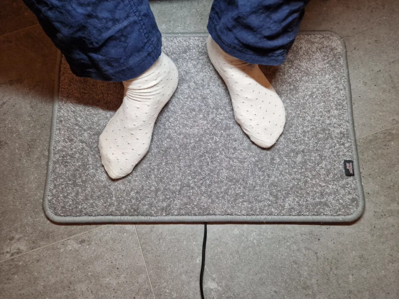 Bovenaanzicht lichtgrijze verwarmde voetenmat met voeten en stekkersnoer met aan/uit-schakelaar
