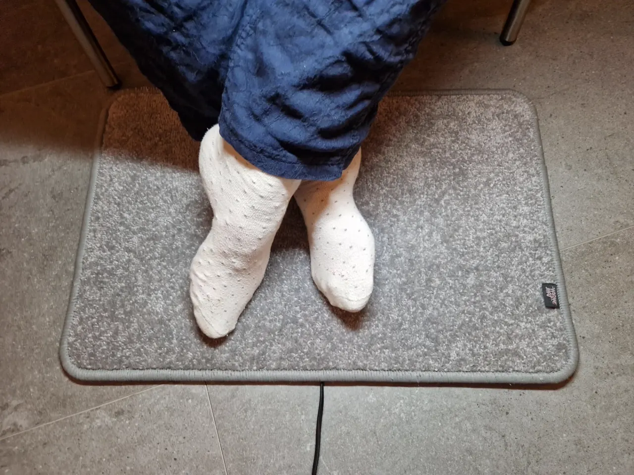 Gekruiste voeten in sokken op de lichtgrijze verwarmde voetenmat Excellent van De WarmeMat™