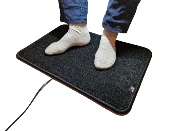 Zwarte verwarmde voetenmat Excellent van De WarmeMat™ met voeten in sokken, hoogpolig en 35~45°C warm
