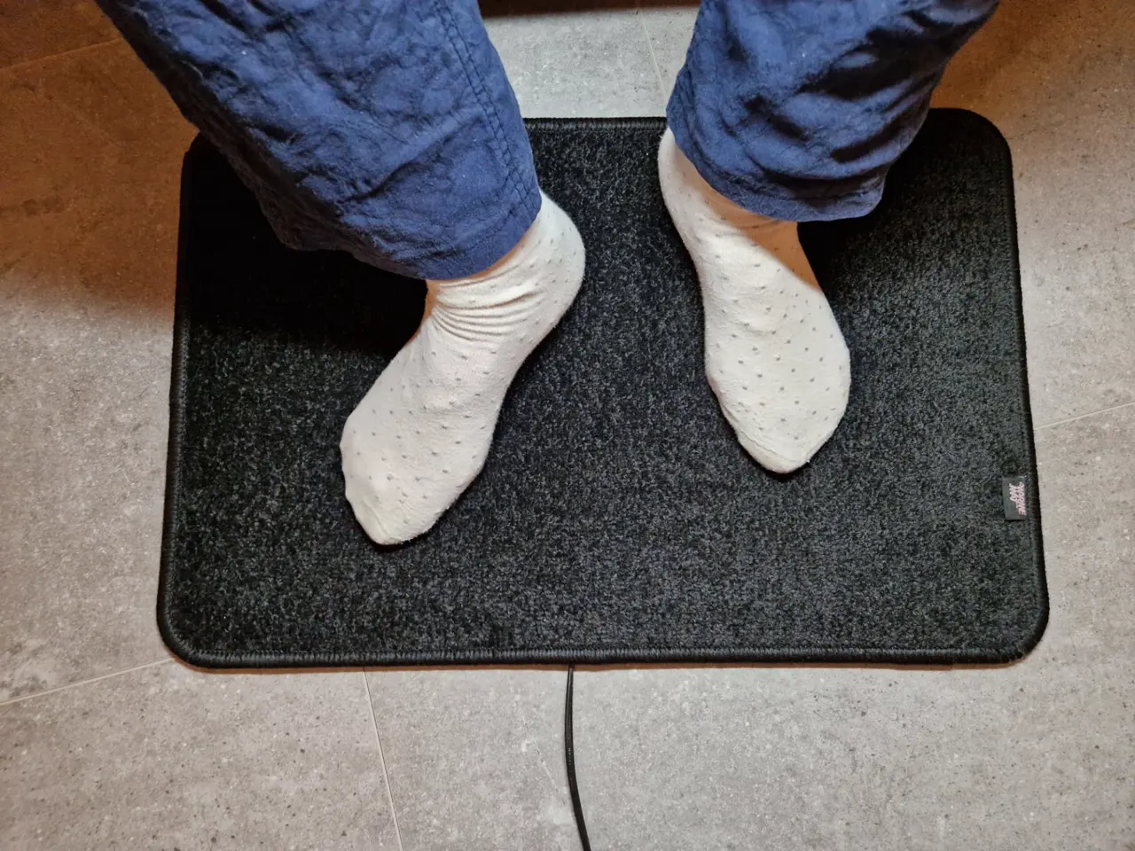Bovenaanzicht zwarte verwarmde voetenmat met fluweelzacht hoogpolig tapijt en voeten in sokken