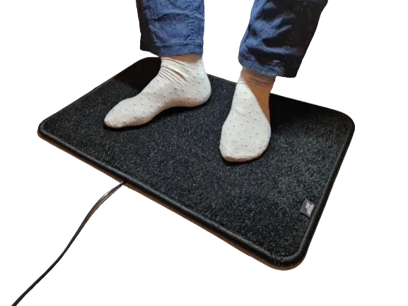 Zwarte verwarmde voetenmat Excellent met voeten in sokken, productfoto op witte achtergrond