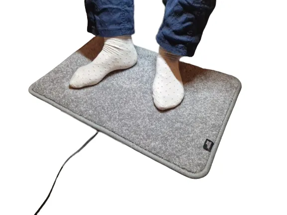 Lichtgrijze verwarmde voetenmat Excellent van De WarmeMat™ met voeten in sokken, hoogpolig en 35~45°C warm